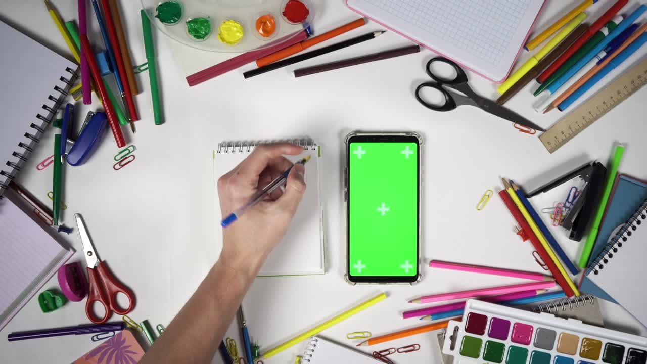 hombre tomar y poner el cuaderno con teléfono inteligente en la mesa cubierta por suministros escolares