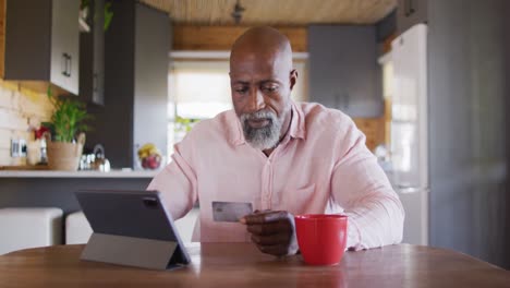 happy senior african american man in log cabin, using tablet for online shopping, slow motion