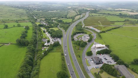 Drone-view-of-the-A30-traffic-in-the-rural-Devonshire-countryside-UK,-surrounded-by-green-fields-and-landscape