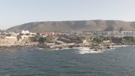 Paisaje-Marino-Con-Montañas-Escénicas-Y-Barrio-Costero-En-Sudáfrica---Toma-Aérea-De-Drones