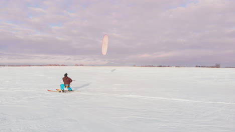 a man is skiing in the snow in a field at sunset. his parachute pulls. kite surfing in the snow..