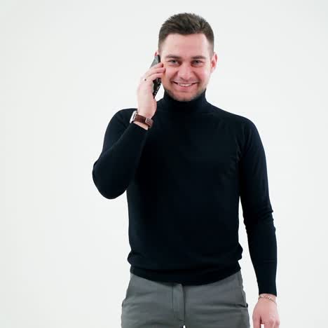 Portrait of a smiling man talking on the phone. Handsome businessman in black sweater talking on a mobile phone isolated in white studio.