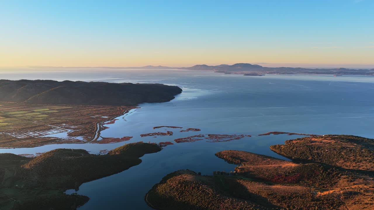 Aerial drone view of Ksamil, Albania surroundings, revealing winding waterways, small islands, shallow wetlands, and the coastal landscape during warm sunrise light