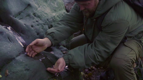 hombre bebiendo agua fresca de manantial después de una caminata exhausta en las montañas