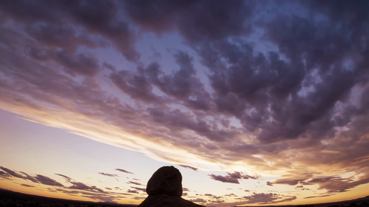 Dramatic wide-angle video shot of a silhouetted rock against a vibrant sunset sky