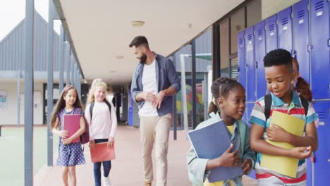 diverse male teacher and happy schoolchildren walking at school