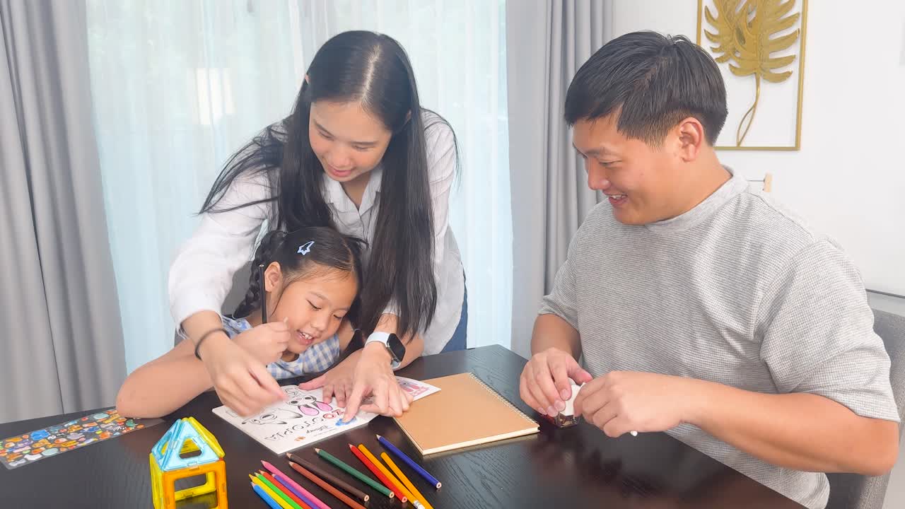 Parents assist young daughter with coloring homework at home. Bright, warm lighting enhances the joyful, collaborative atmosphere