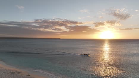 speedboat drives off coast of sandy white shores as sunset light casts ray over water