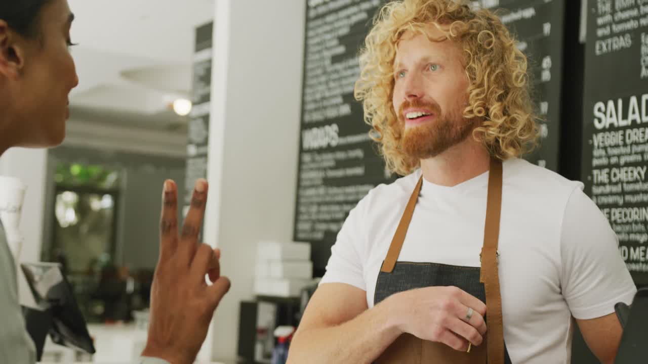 Donna felice di diverse origini che compra il caffè e chiacchiera con un barista in un bar.