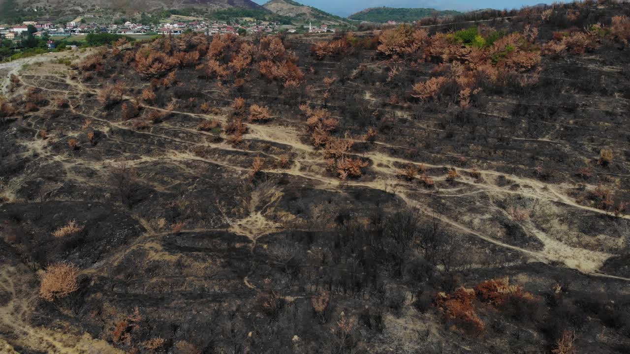 Burned land on hills near city, black devastated surface with burnt trees and grass