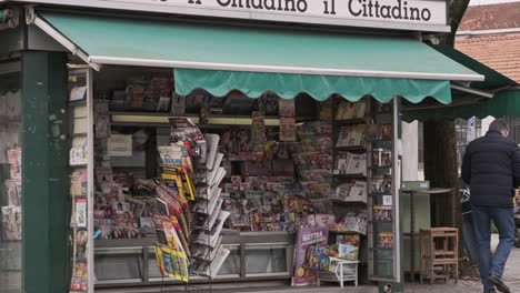 Adult Man Wearing Face Mask Due To Pandemic Buying Newspaper And Leaving From A Newsstand In Town In Milan, Italy. - wide slow motion