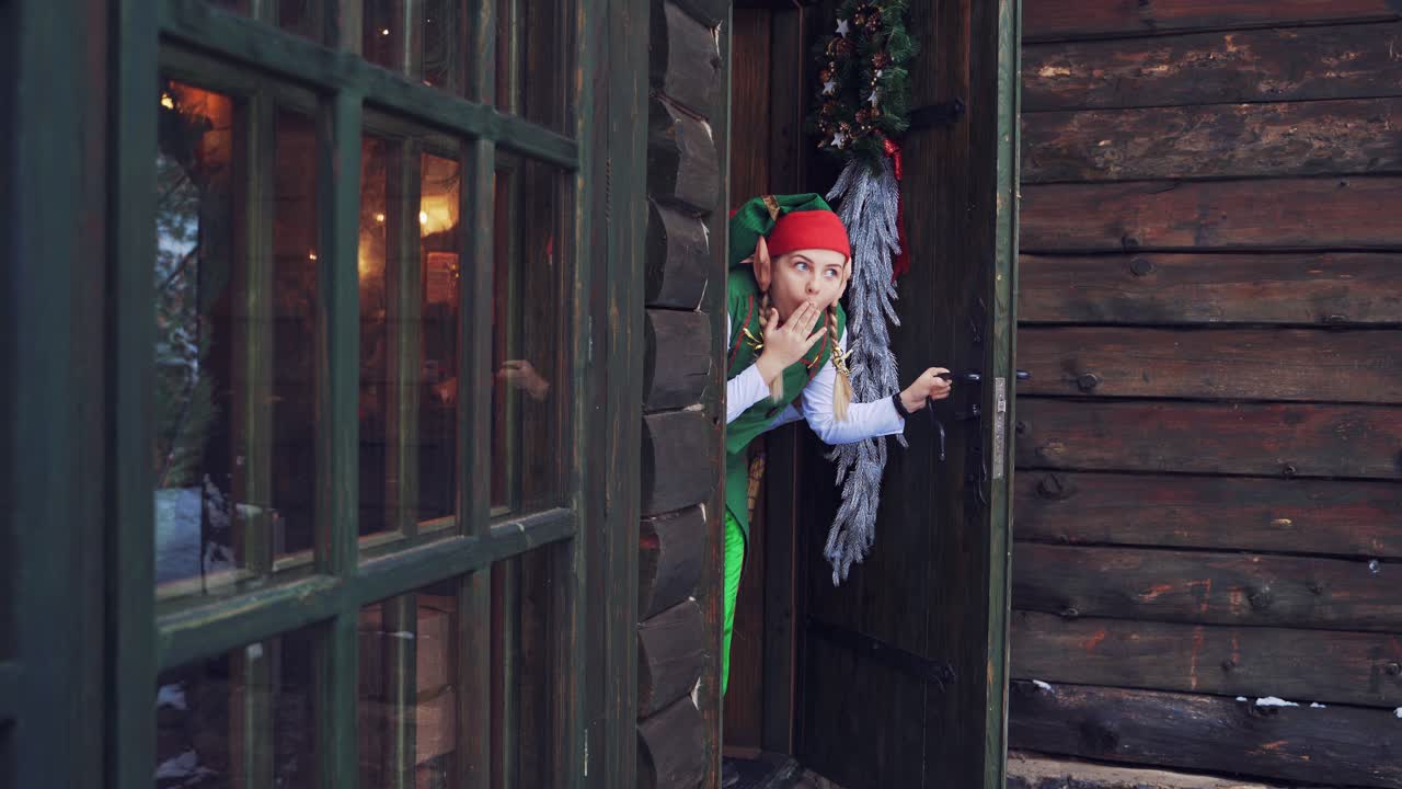 Happy elves peeking out from behind the door and laugh joyfully. Young female elf opens the front door inside the house.