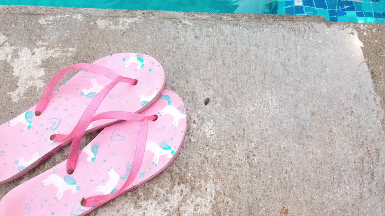 Pink flip-flops on the ground near a pool, with a blue tiled edge in the background