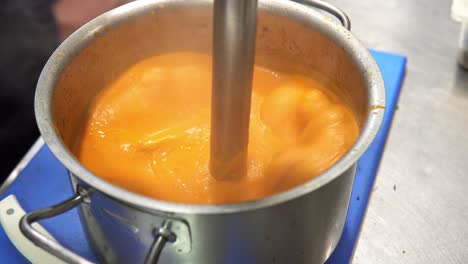 close-up of orange cream sauce being whipped in a hot pot with smoke coming out of it