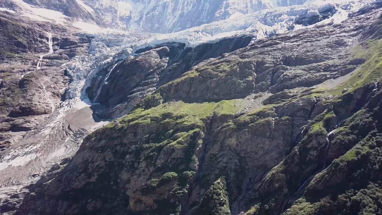 Panoramica aerea laterale delle Alpi svizzere con un ghiacciaio e una cascata.
