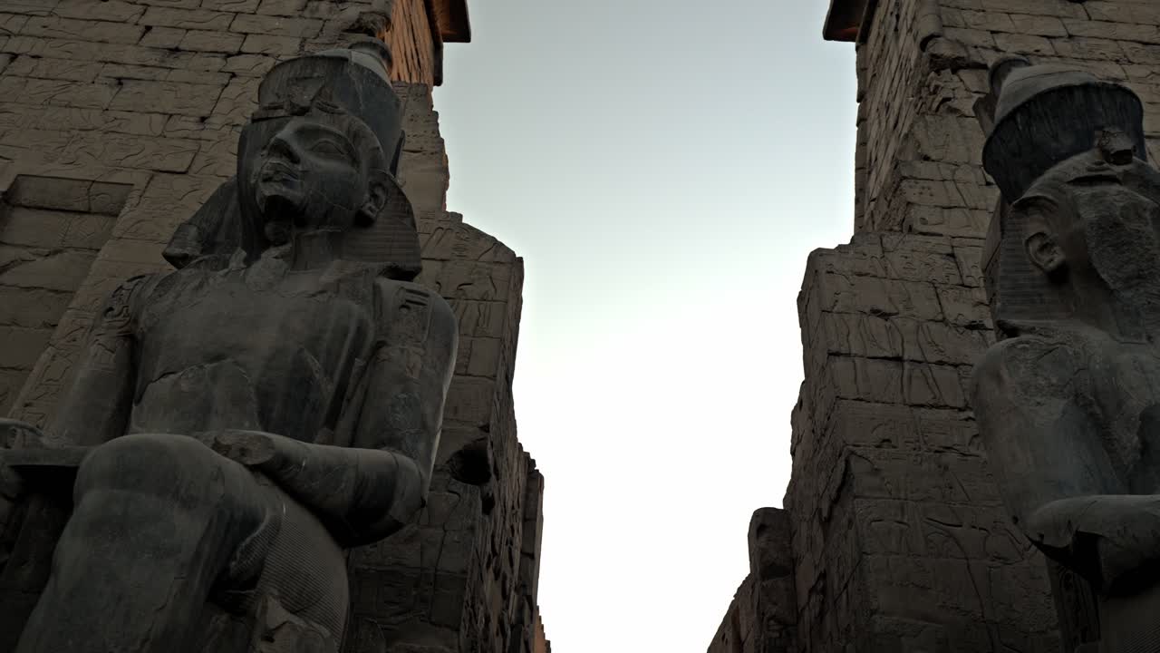 Masivní sedící sochy Ramesse II., které střeží vstup do chrámu. Vytesané z tmavé žuly, tyto postavy zobrazují faraona nosícího Dvojitou korunu Horního a Dolního Egypta.
