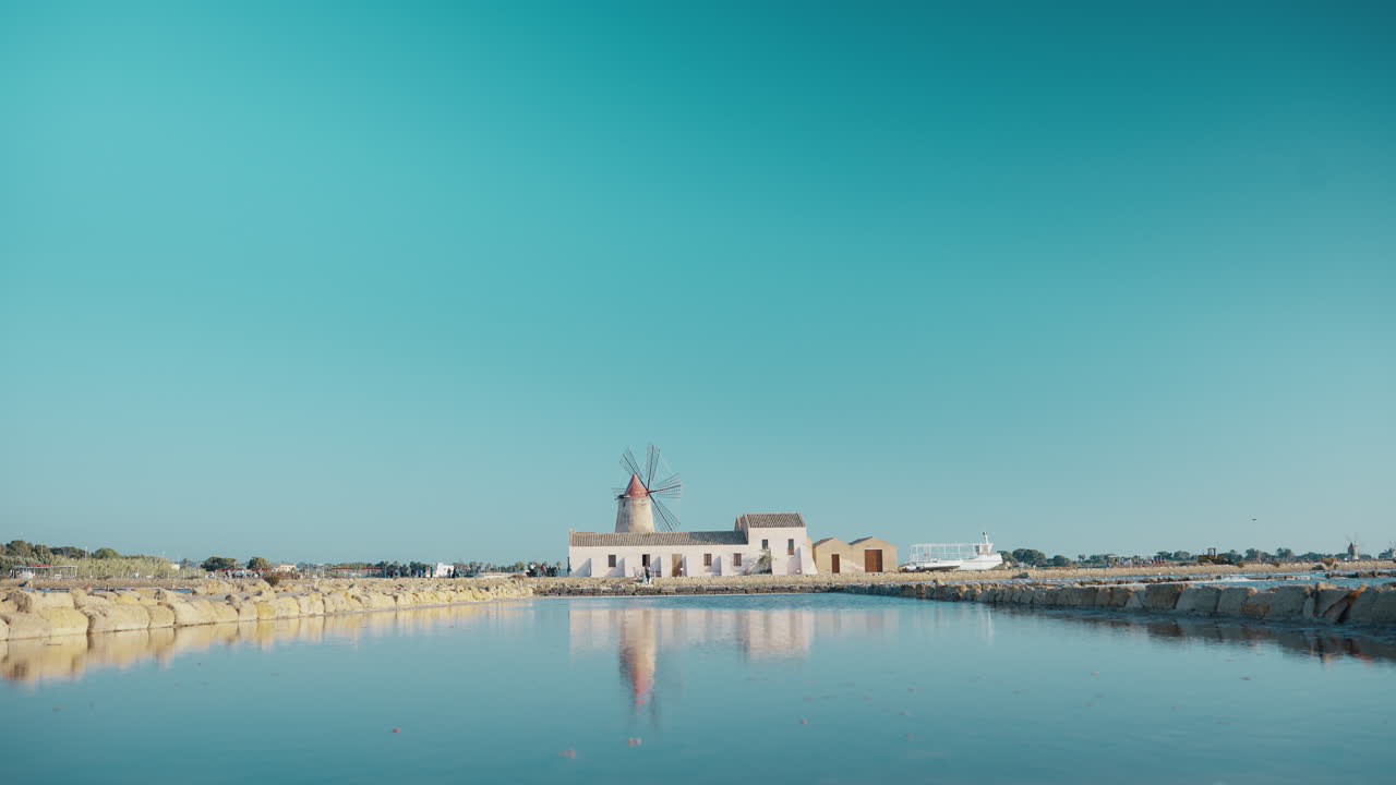Dataran garam Marsala dengan kincir angin dan laguna yang tenang, Stagnone, Sisilia, Italia