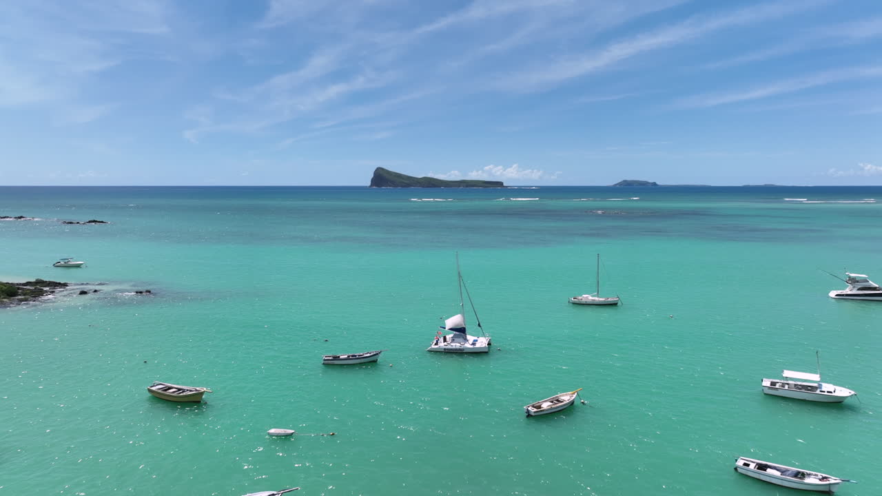 Drone shot in Mauritius, Cap Malheureux. The camera passes a tree in the foreground, revealing anchored yachts on an emerald ocean. Gunner’s Quoin Island rising on the calm horizon in the background