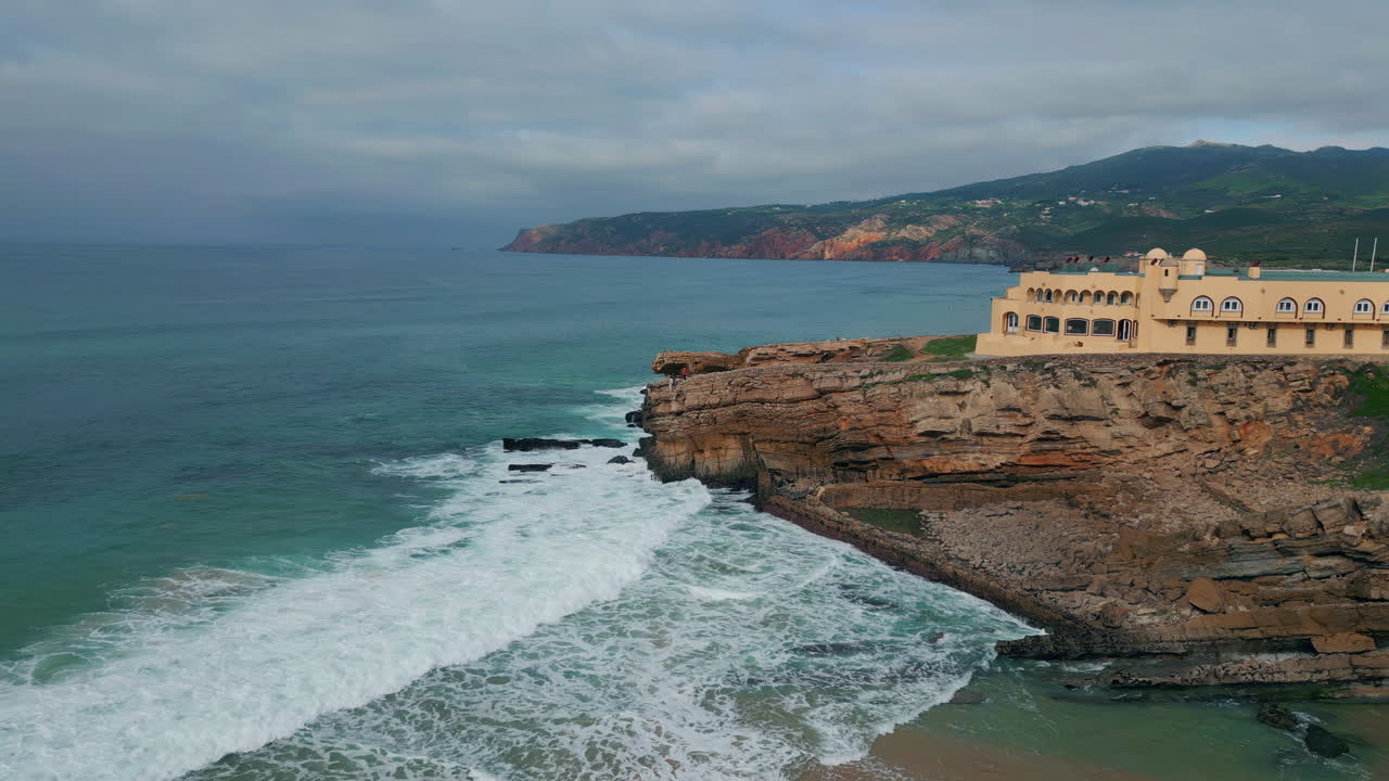 Edificio costiero su scogliere che si affaccia su un mare turbolento. Onde spumeggianti, ripresa aerea