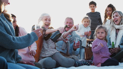 multi-generation family opening bottle and pouring drinks on winter beach vacation