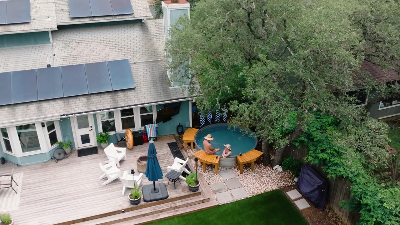 Aerial drone orbit pull away of couple sitting in hot tub in dream backyard, deck, and lush oak trees. home property listings, luxury lifestyle content, and outdoor living in Texas suburb