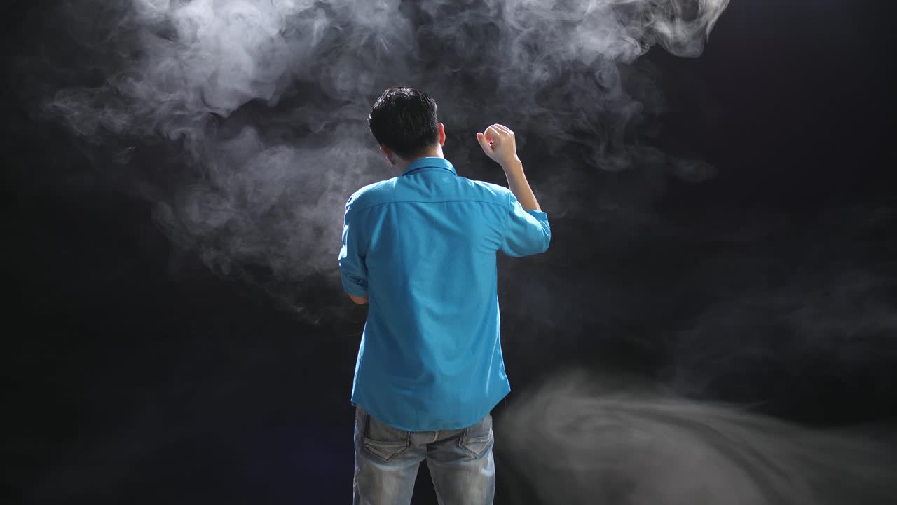 파란 셔츠 를 입은 남자 가 연기 가 가득 찬 스튜디오 에서 포즈 를 취 하고 있다
