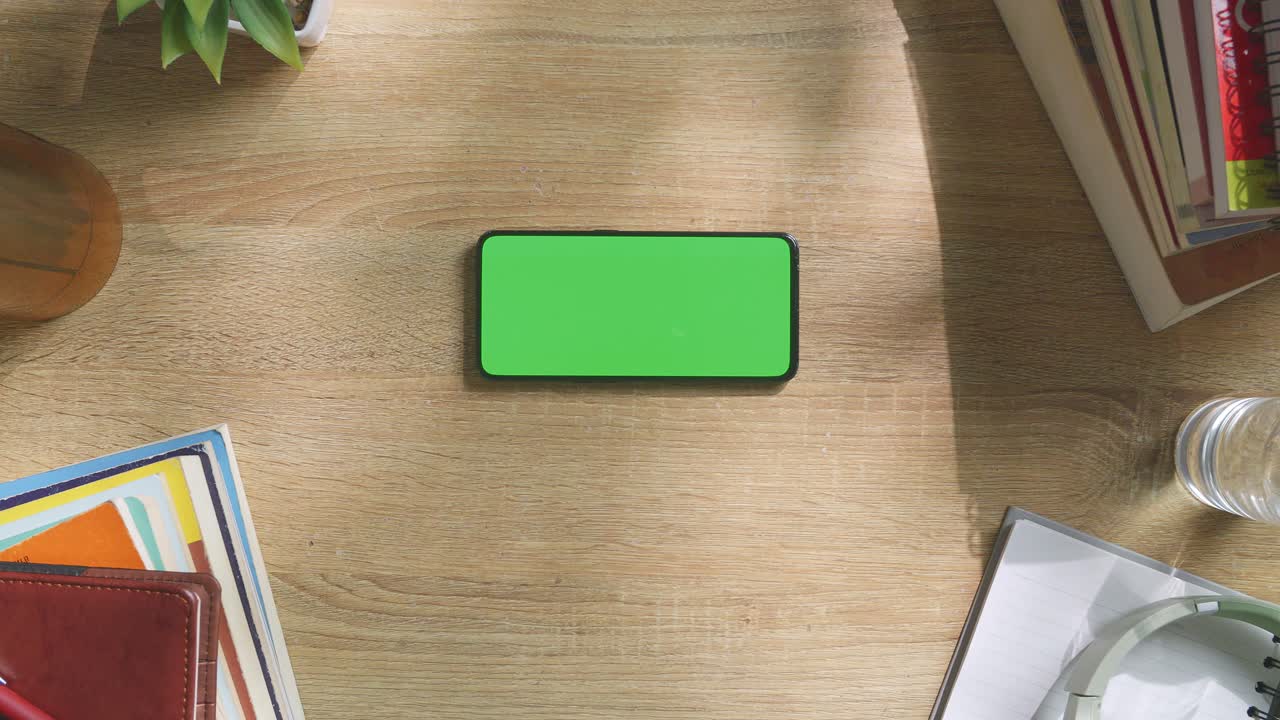 vista de arriba hacia abajo de una computadora portátil con pantalla verde simulada pantalla chromakey en un escritorio de oficina de madera al lado de la libreta con bolígrafos, gafas y un vaso de agua.