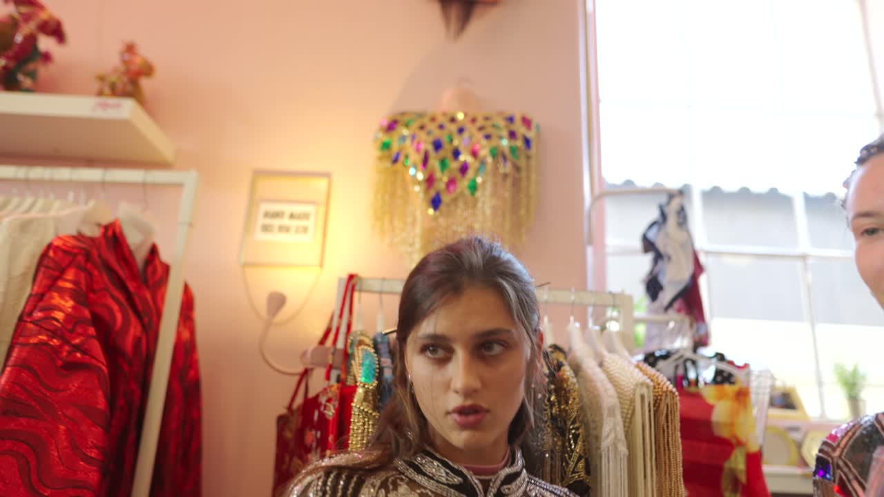 Two women modeling embellished capes in a boutique