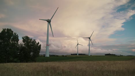 three wind turbines with rotating blades on green field, full shot