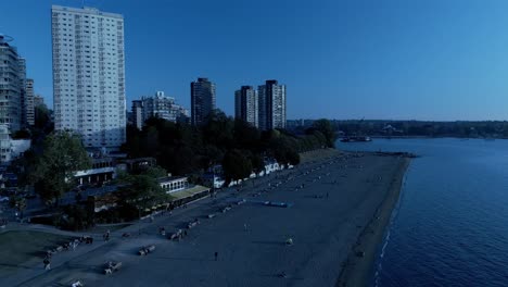 english bay sunset beach reveal pan drone overlooking commercial properties of davie and denman pubs restaurants condominiums apartments hotels shops sunny summer day skyline lush greenery post modern