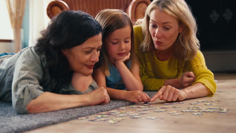 same sex family with two mature mums and daughter lying on floor doing jigsaw puzzle at home