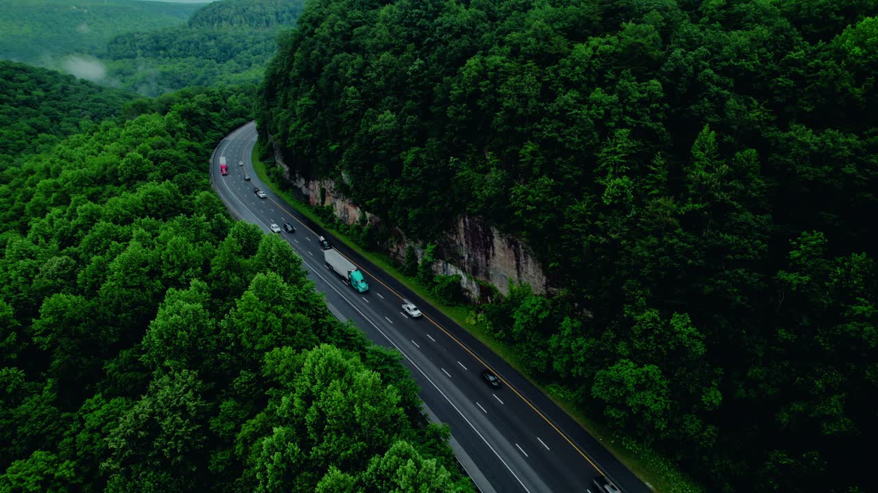 Semi trucks winding through Tennessee's Monteagle Pass, surrounded by dense forest and towering rock walls.