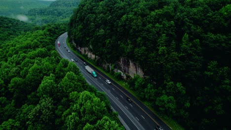 semi trucks winding through tennessee's monteagle pass, surrounded by dense forest and towering rock walls.