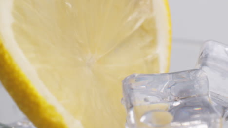 kaltes, frisches sprudelwasser, das mit eis und zitronenscheiben in ein glas gegossen wird