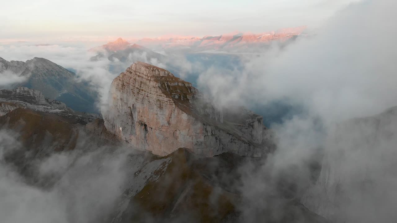 Aerial hyperlase view of Tour de Mayen and Tour d'Aï in Leysin, Vaud, Switzerland with clouds flowing past the mountain peaks and cliffs with a colorful alpenglow on the Swiss Alps in the background