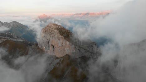 Vista-Aérea-Hiperlase-Del-Tour-De-Mayen-Y-Tour-D&#39;aï-En-Leysin,-Vaud,-Suiza-Con-Nubes-Que-Fluyen-Más-Allá-De-Los-Picos-De-Las-Montañas-Y-Acantilados-Con-Un-Colorido-Alpenglow-En-Los-Alpes-Suizos-Al-Fondo