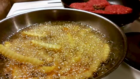 french fries floating in a bubbling hot oil with burgers in the background, slomo