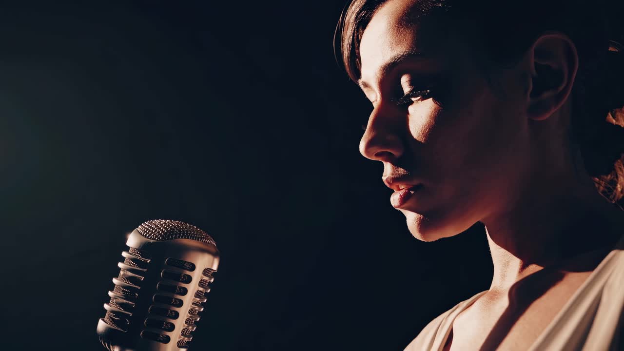 Close-up, side-angle shot of a vintage microphone and singer under dramatic lighting