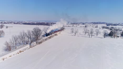 Vista-Aérea-De-Una-Antigua-Locomotora-De-Vapor-Que-Se-Acerca-Tirando-De-Los-Coches-De-Pasajeros-Y-Soplando-Humo-Y-Vapor-Durante-La-Hora-Dorada-A-última-Hora-De-La-Tarde