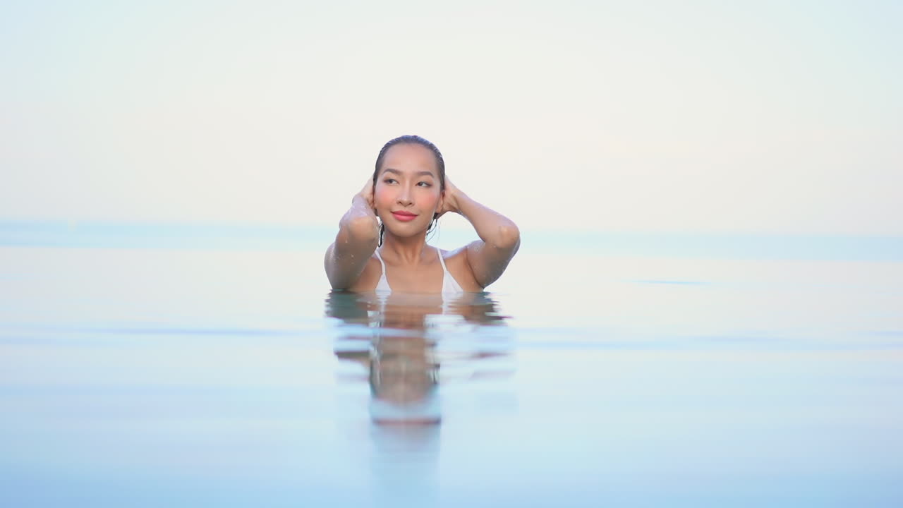 수영장에서 가슴 높이의 아름다운 여성이 젖은 머리카락을 얼굴에서 밀어냅니다.