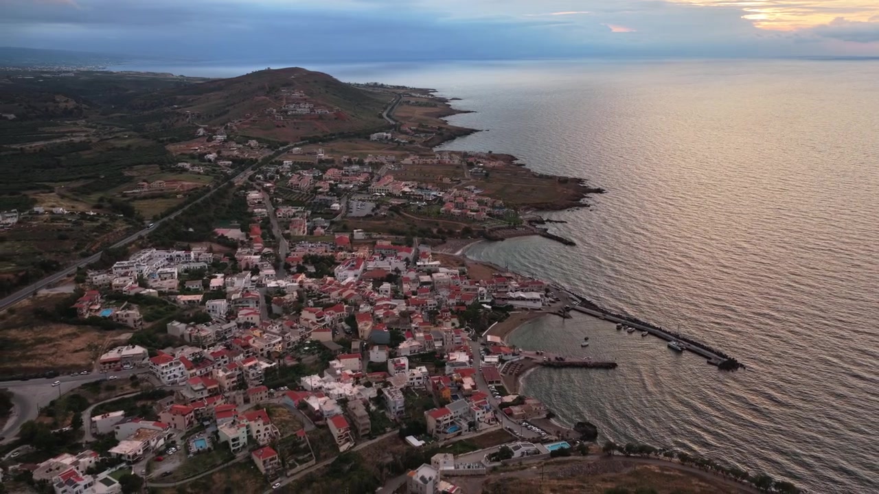 Vista aérea de drone de uma cidade costeira e seu pequeno porto abaixo de um promontório árido, Panormos, Grécia