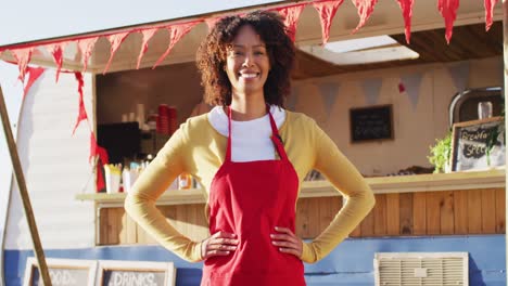 Portrait-of-african-american-woman-with-arms-on-hips-smiling-while-standing-near-the-food-truck