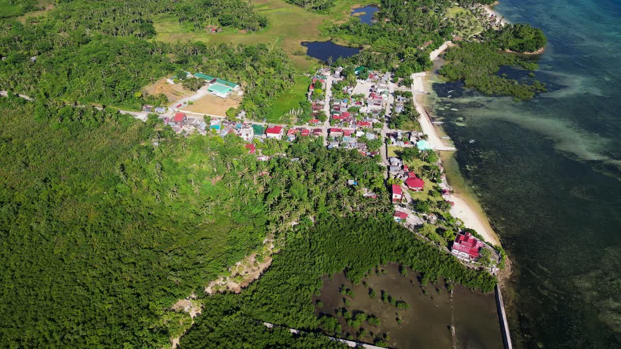 Picturesque aerial view of coastal barangay community amid lush tropical island setting and turquoise cove at Catanduanes, Philippines.
