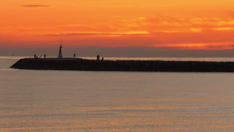 people fishing on sea wall at dawn under orange skies
