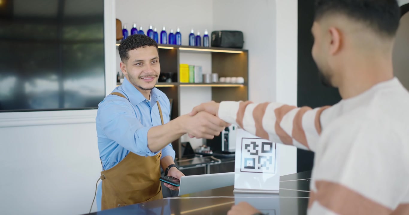 Barista afroamericano che mostra un lettore di carte per il pagamento, mentre un cliente tocca vicino al codice QR.