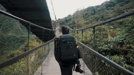 cruce de mochileros en puente suspendido sobre la cascada pailon del diablo en baños, ecuador