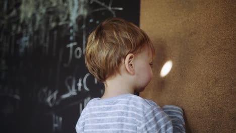 Toddler-boy-stands-playing-with-light-mark-on-wall-in-wooden-hut,-happy