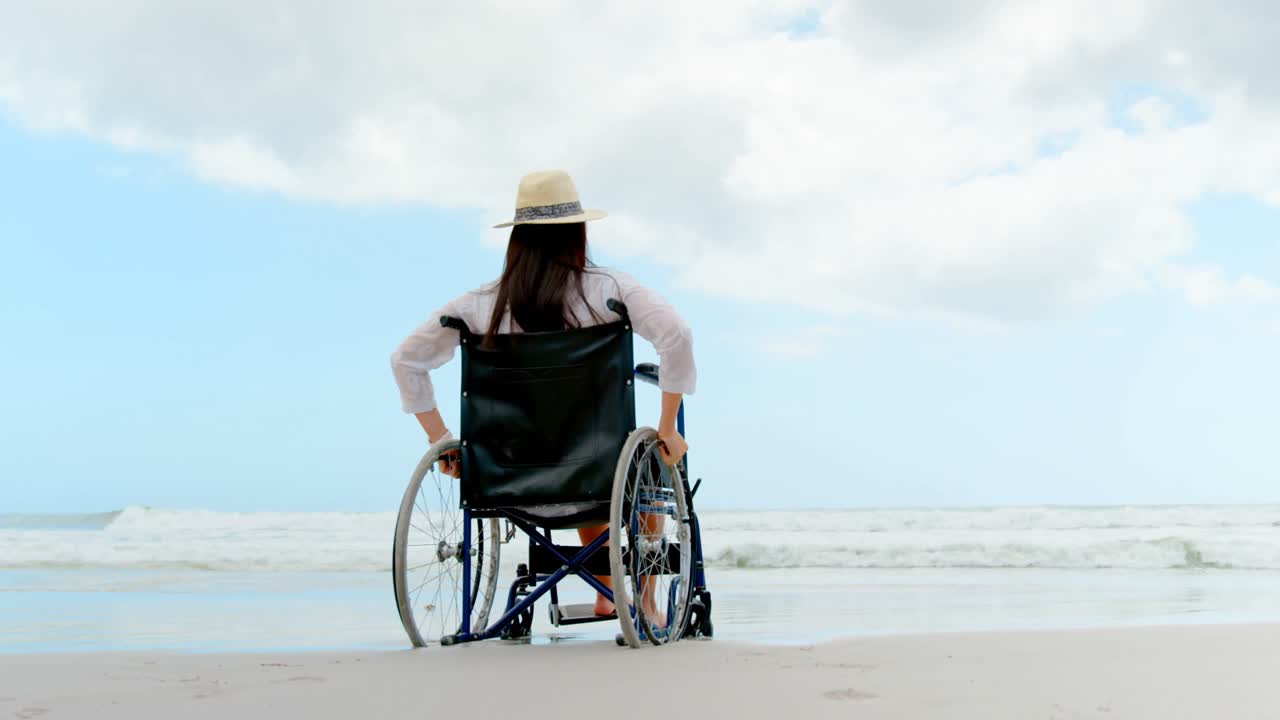 Rear view of disabled woman sitting on wheelchair at beach 4k