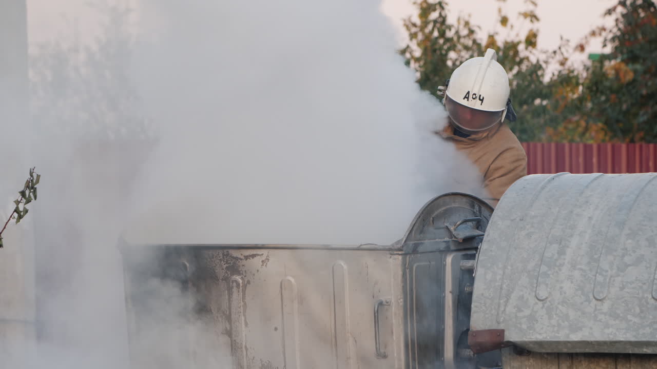 Il pompiere spegne un incendio vicino ai bidoni della spazzatura dopo una rivolta.