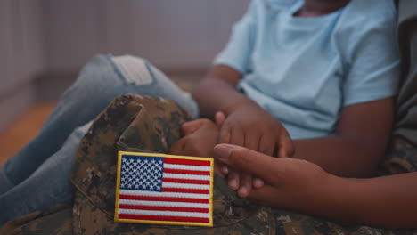 close up of american army mother in uniform home on leave hugging son sitting on floor in kitchen